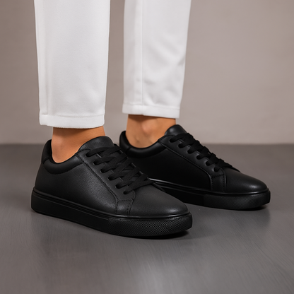 Black sneakers worn with white pants on a neutral background