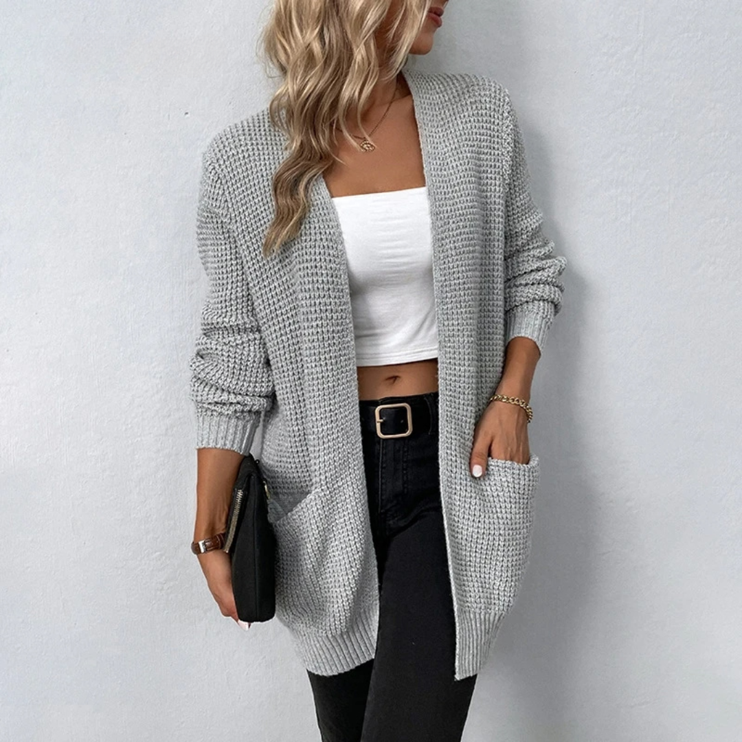 Woman wearing a long gray cardigan over a white top and black pants on a light gray background