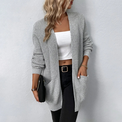 Woman wearing a long gray cardigan over a white top and black pants on a light gray background